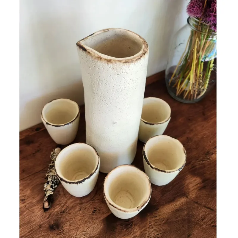 Set de sour: jarra alta de gres claro rodeada de seis vasos con borde oscuro