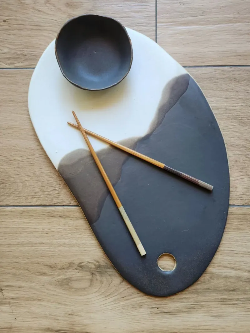 Tabla de gres ovalada blanco y negro con un pocillo negro y palillos